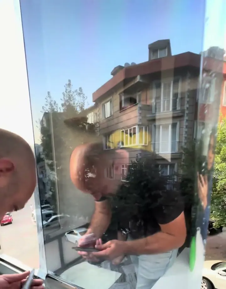 Aynalı cam filmi rakle ile cama yerleştirilirken; filmde karşı bina yansıyor